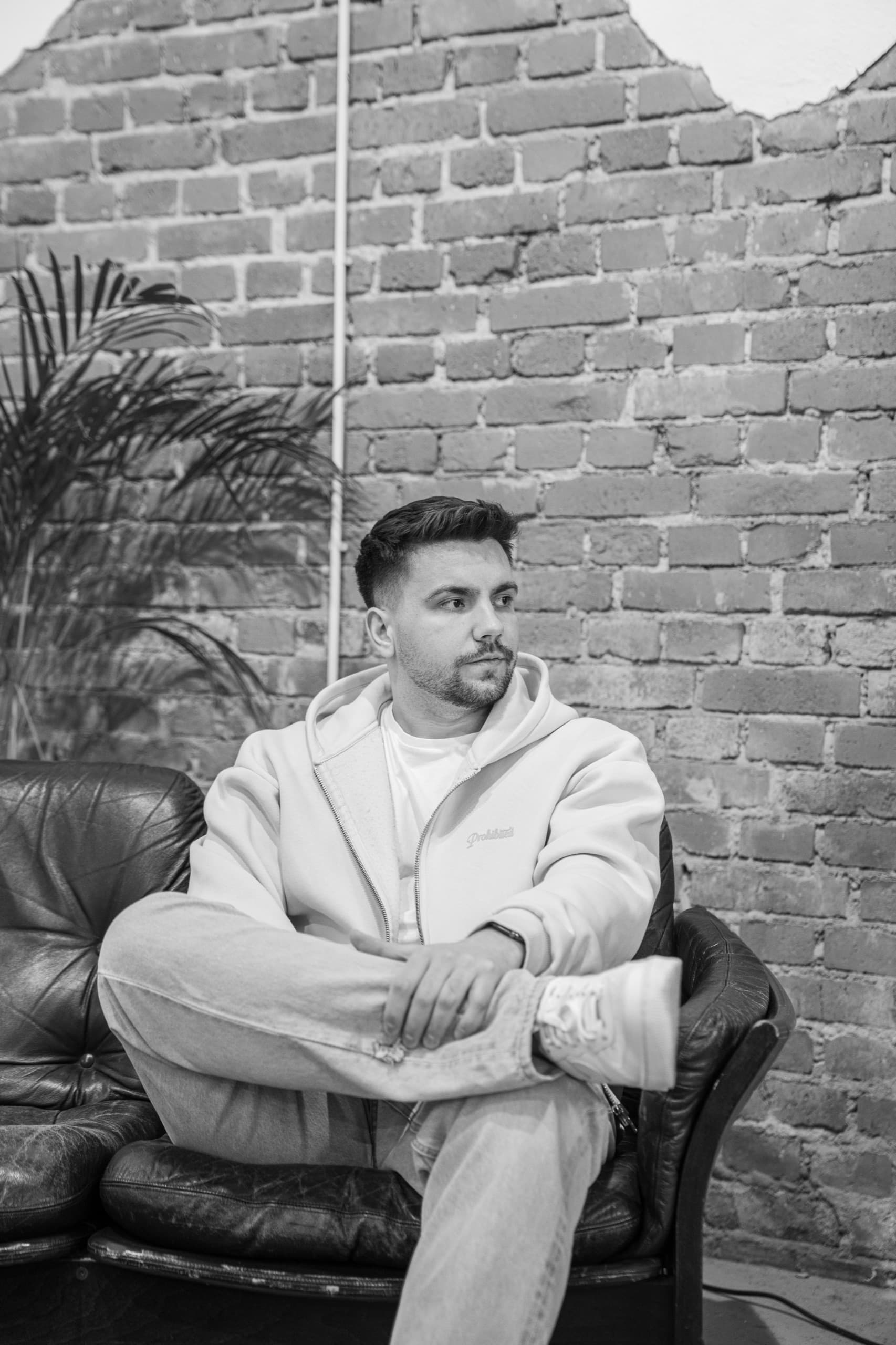 DJ MVM — Portrait auf Ledersofa vor Backsteinwand